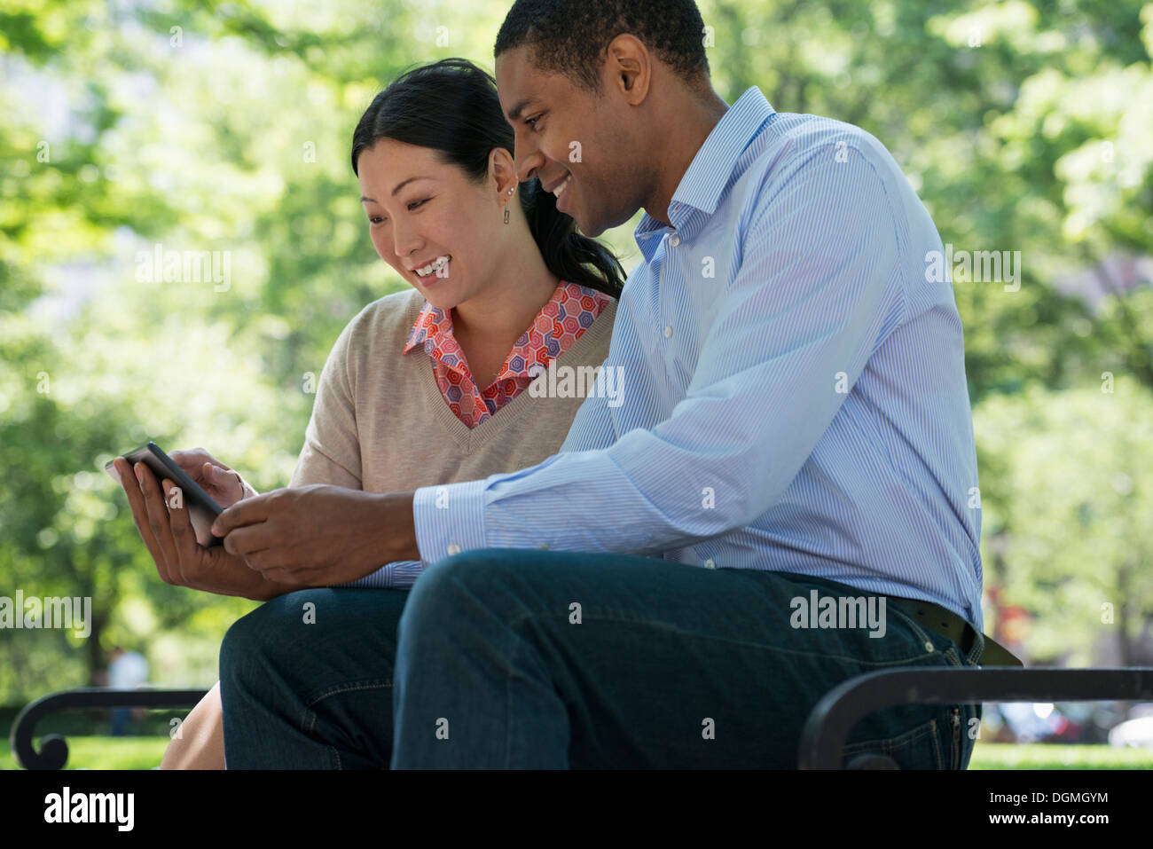 L'été. Les gens d'affaires. Un homme et une femme assis sur un banc, à l'aide d'un téléphone intelligent. Banque D'Images