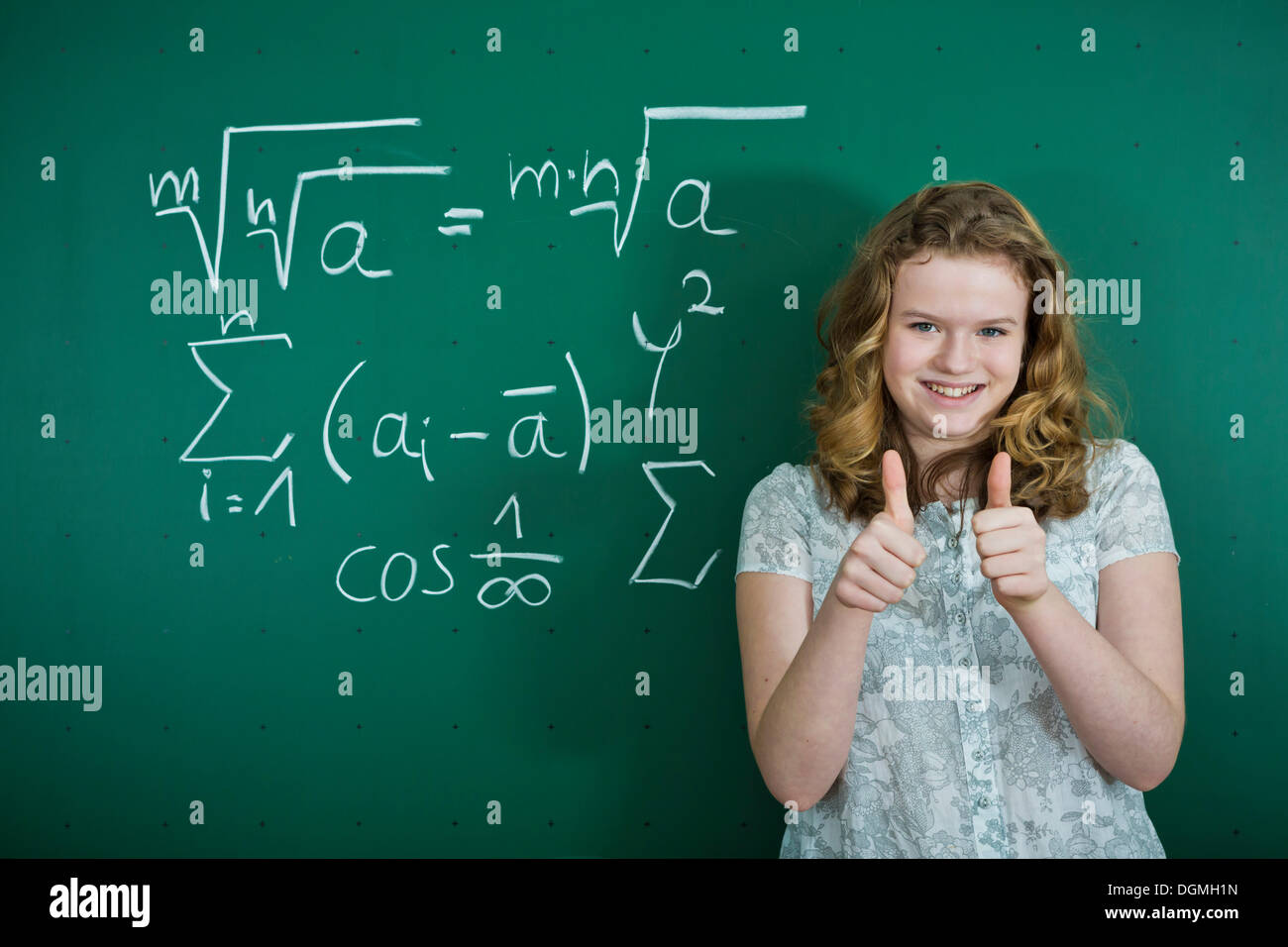 Lycéenne debout devant un tableau noir de l'école avec des formules mathématiques, faisant un geste vers le pouce, Allemagne Banque D'Images