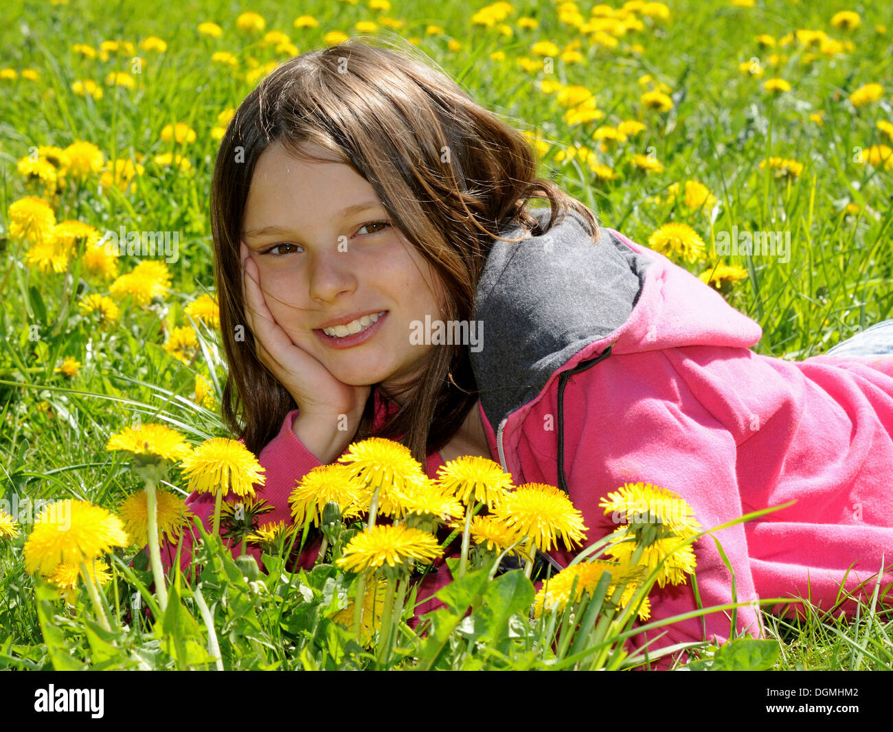 Fille, 12 ans, allongé dans un champ de pissenlit, smiling Banque D'Images