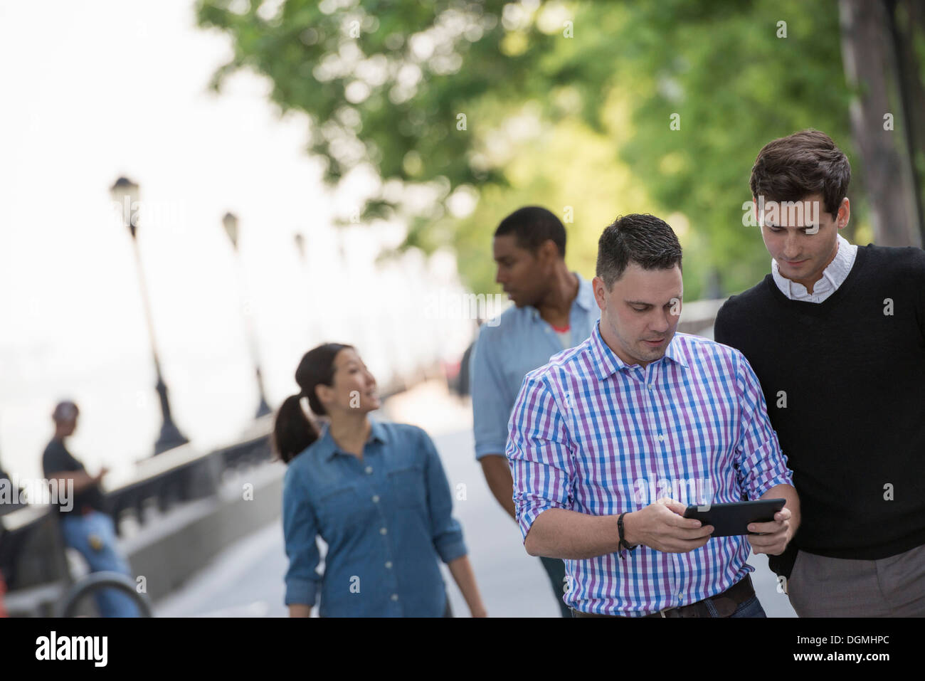 L'été dans la ville. Quatre personnes dans un groupe. L'un en utilisant sa tablette numérique. Banque D'Images