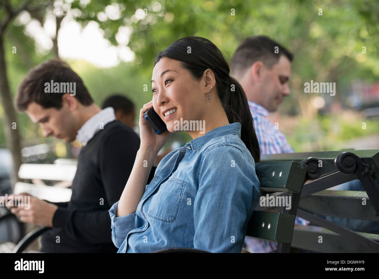 L'été dans la ville. Une femme et trois hommes assis dans le parc, chacun sur leur propre téléphone ou à l'aide d'une tablette. Banque D'Images