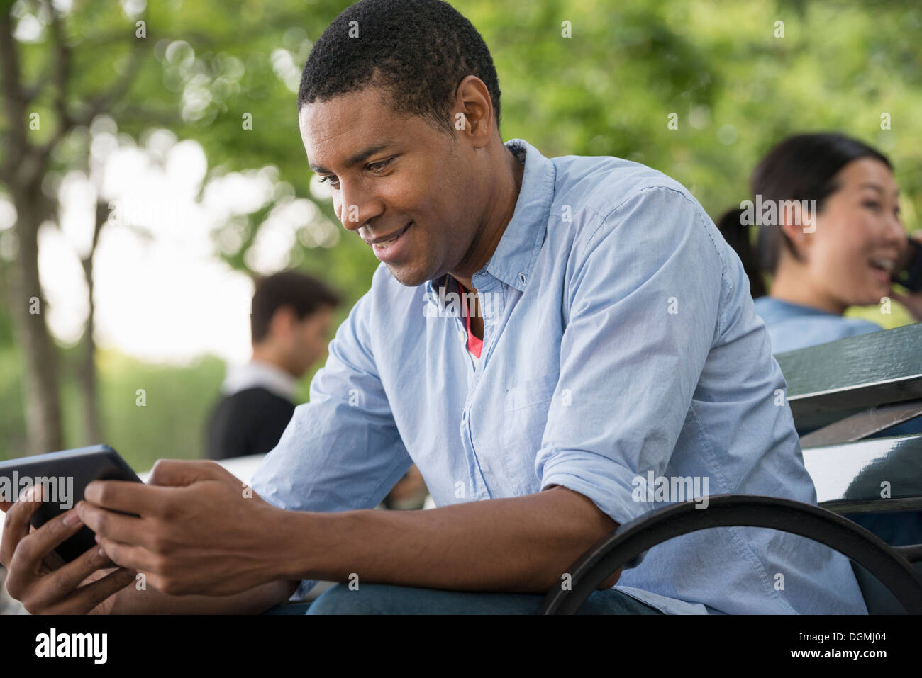 L'été. Un homme assis sur un banc à l'aide d'une tablette numérique. Banque D'Images