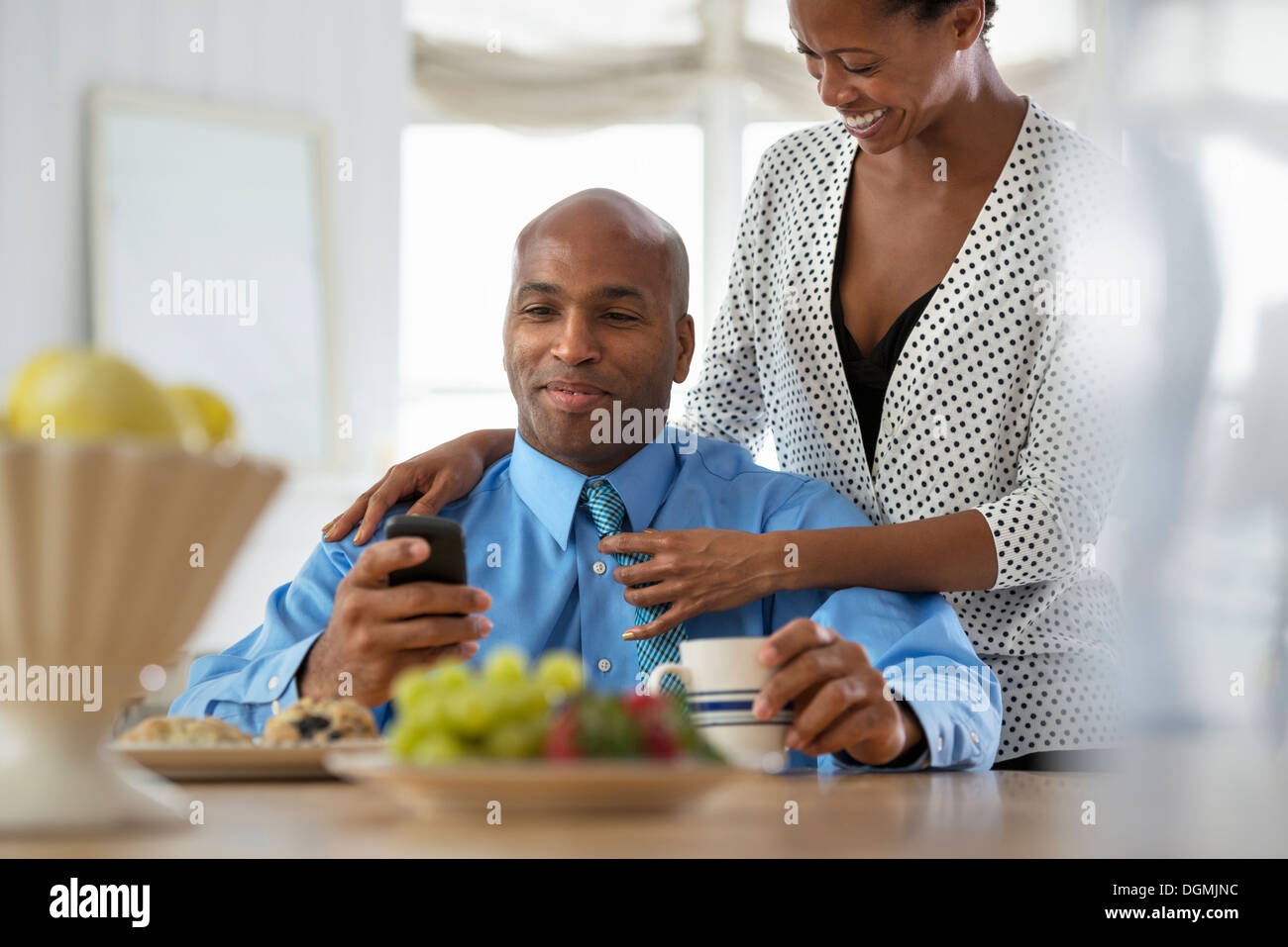 Un homme en chemise bleue, assis à un bar de petit-déjeuner à l'aide d'un téléphone intelligent. Banque D'Images