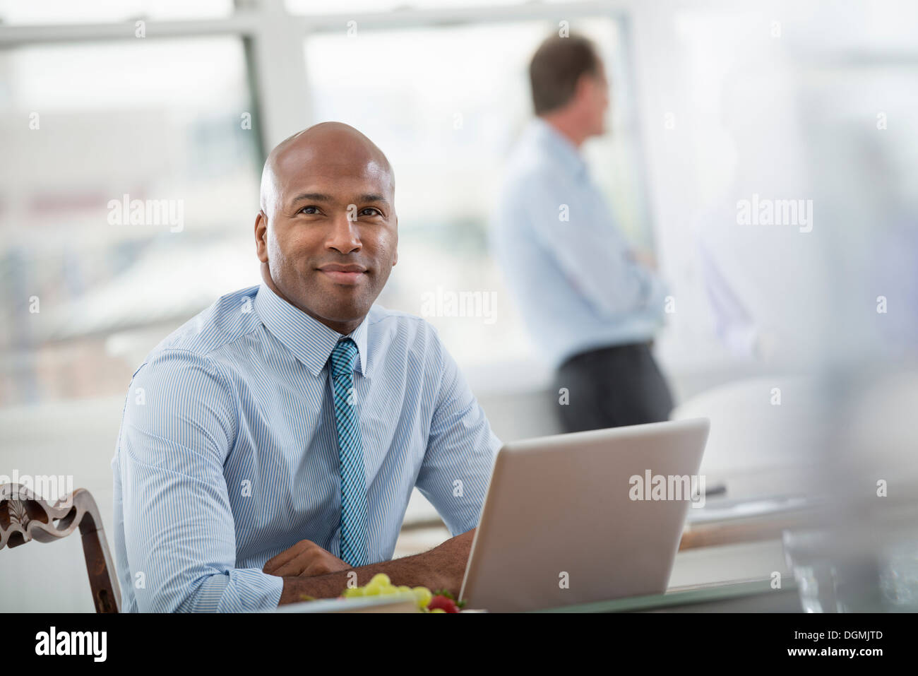 La vie de bureau. En homme d'une chemise et cravate assis à un bureau, à l'aide d'un ordinateur portable. Banque D'Images