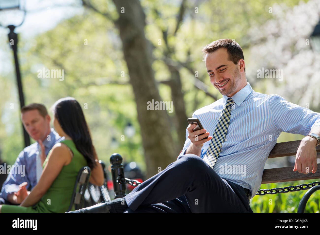 Un couple sur un banc à l'arrière-plan, et un homme contrôler son téléphone. Banque D'Images