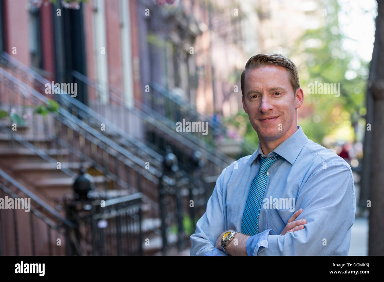 Un homme en chemise bleue et cravate bleue avec les bras croisés, debout sur le trottoir Banque D'Images
