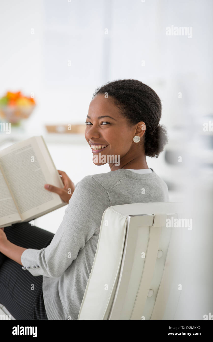 L'entreprise. Une femme assise et la lecture d'un livre. La recherche ou la relaxation. À la par-dessus son épaule et sourit. Banque D'Images