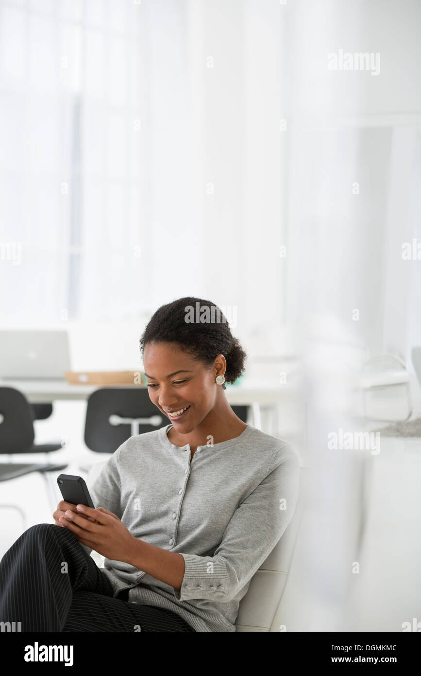 L'entreprise. Une femme assise dans une chaise confortable, contrôler son téléphone intelligent pour les messages. Banque D'Images