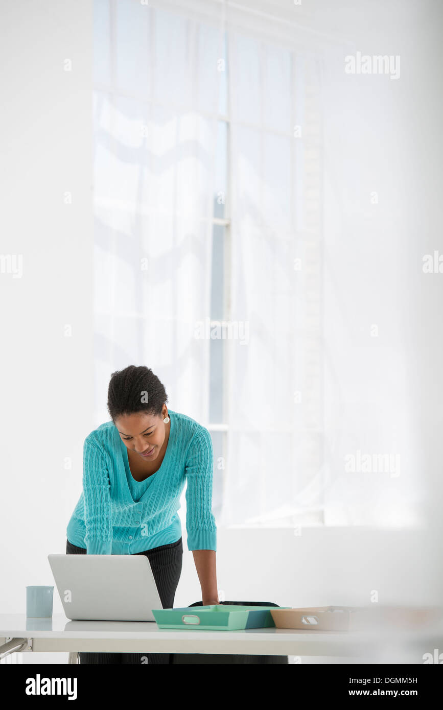 L'entreprise. Une femme se penche au-dessus d'un bureau à l'aide d'un ordinateur portable. Banque D'Images L'entreprise. Une femme se penche au-dessus d'un bureau à l'aide d'un ordinateur portable. Banque D'Images