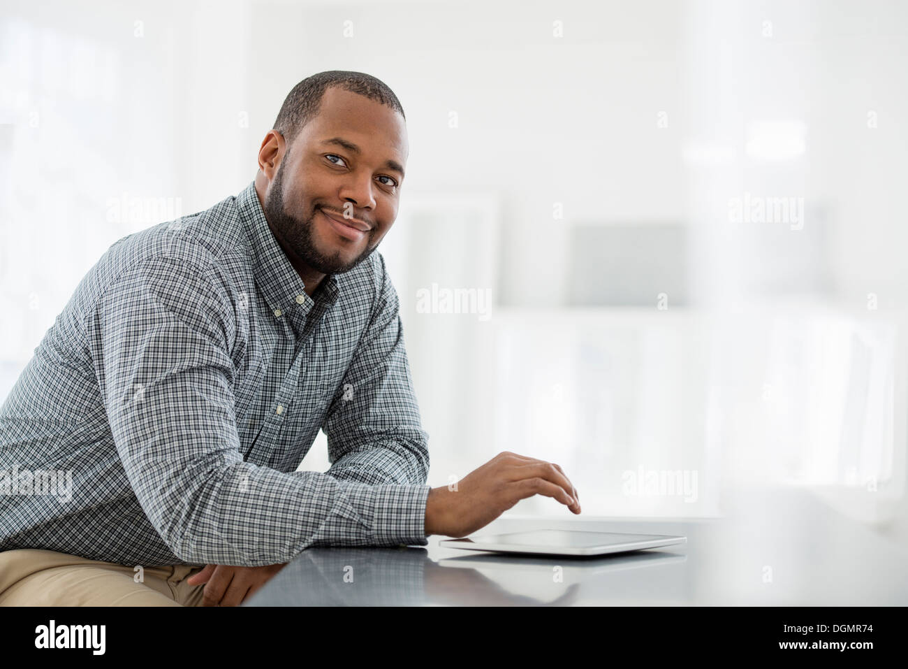 L'intérieur du bureau. Un homme assis à une table, à l'aide d'une tablette numérique. Banque D'Images