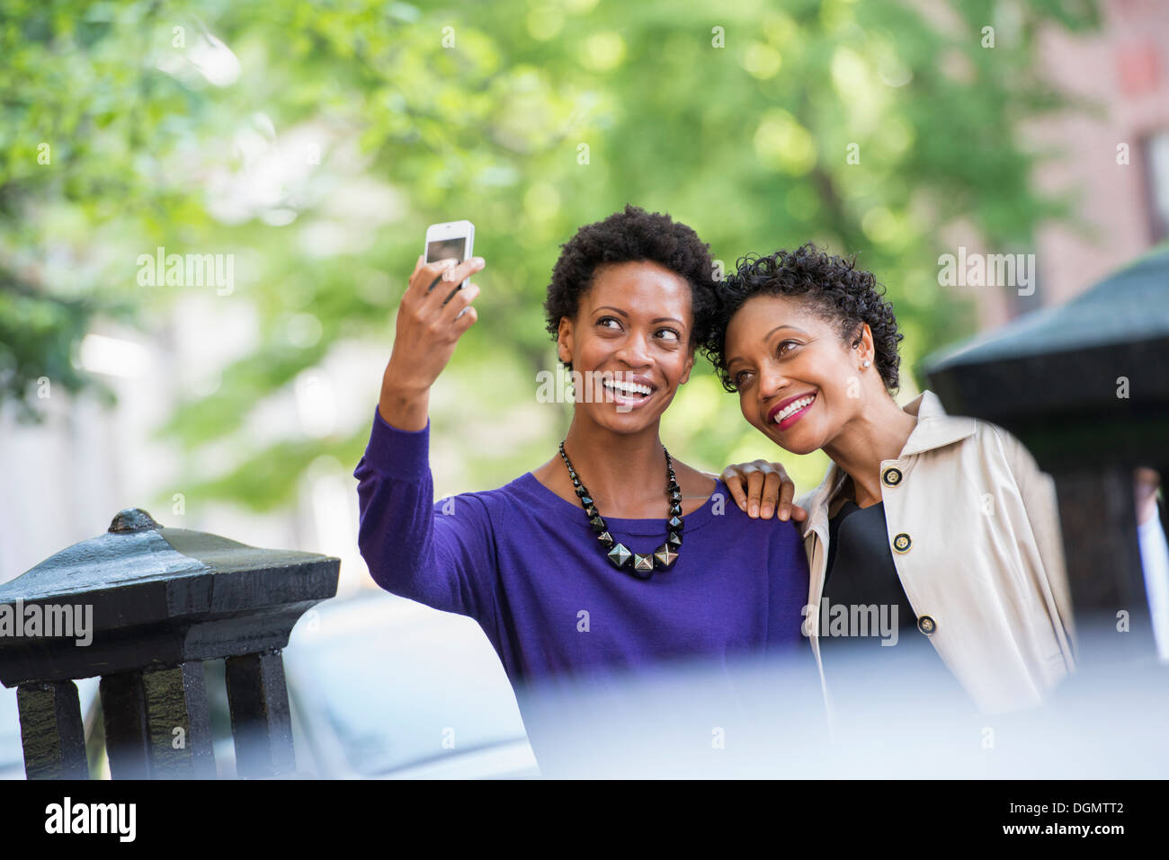 La vie en ville. Deux femmes assises sur un banc de parc, côte à côte. Posant pour une photo avec un téléphone intelligent. Banque D'Images