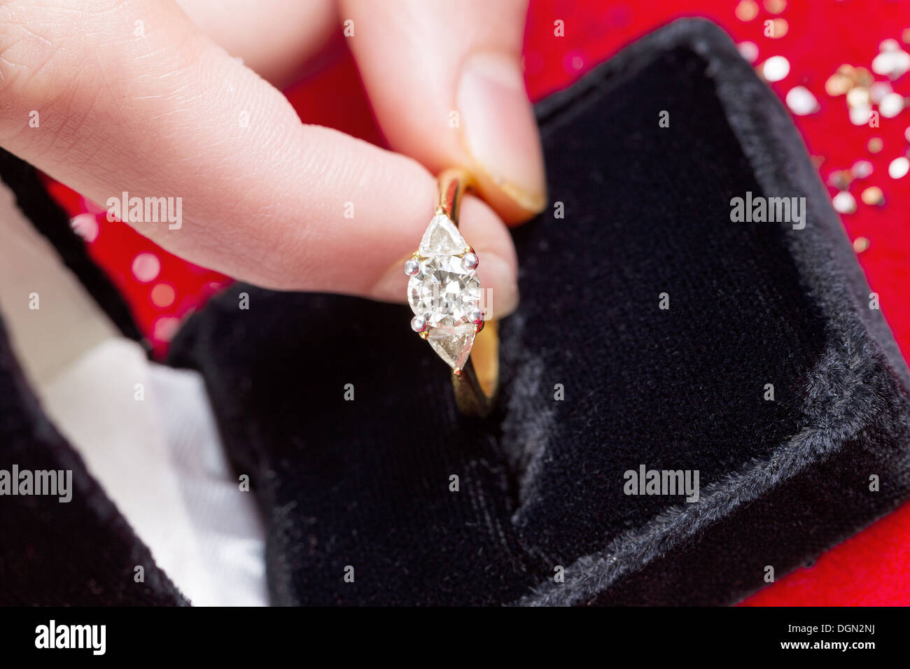 Photo horizontale des doigts féminins ramasser anneau de diamant à partir de la boîte de bijoux sur fond rouge Banque D'Images