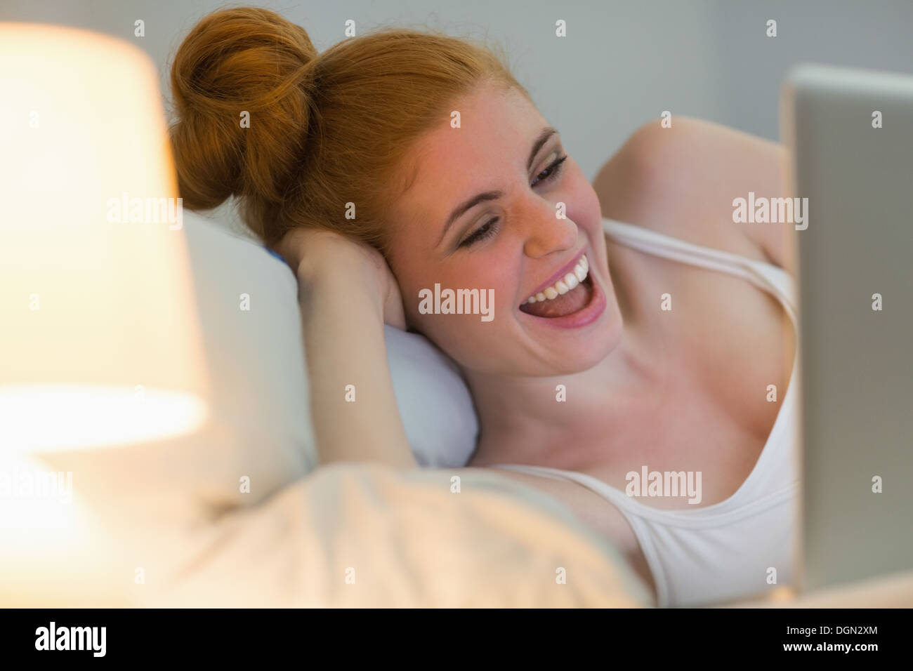 Rire redhead lying on her bed using laptop Banque D'Images