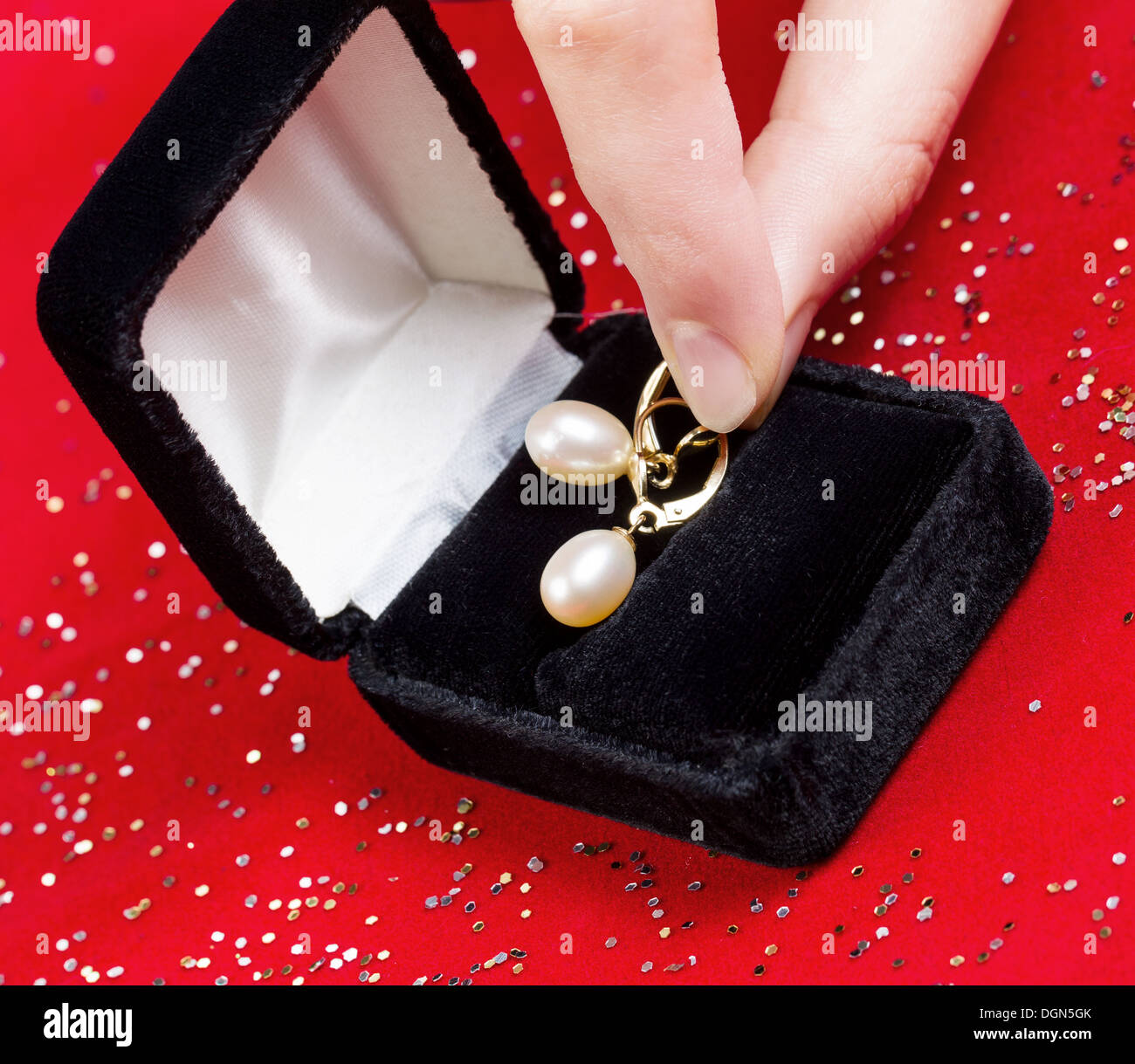 Photo de femme doigts décrochant Pearl Earrings à partir de la boîte de bijoux sur fond rouge Banque D'Images