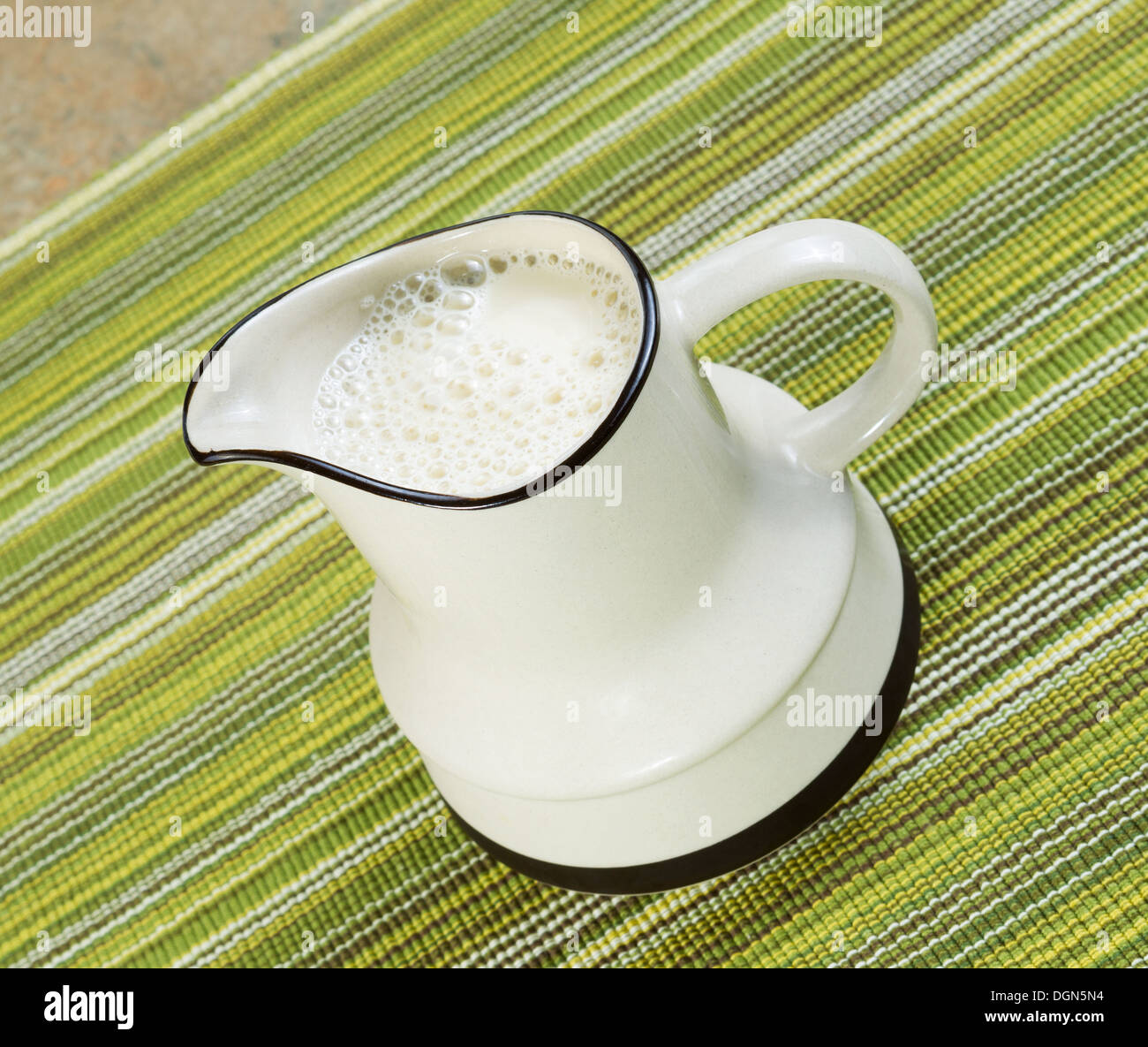 Photo inclinée de lait de soja en pichet blanc avec un chiffon sous la table verte Banque D'Images