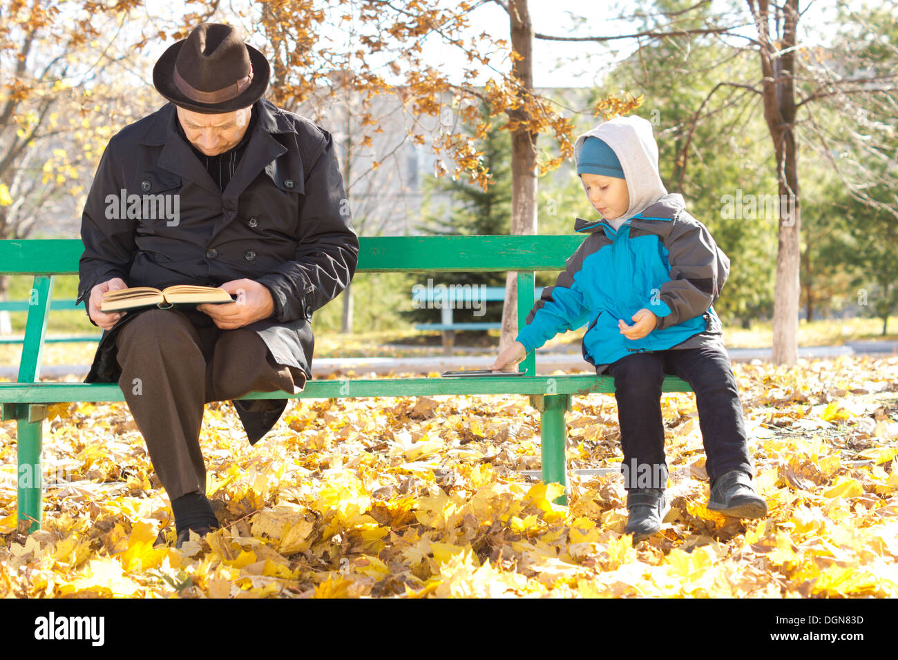 Adorable petit garçon jouant aux côtés de son grand-père que les deux s'asseoir ensemble sur un banc de parc à l'automne soleil vêtu de vêtements chauds. Banque D'Images