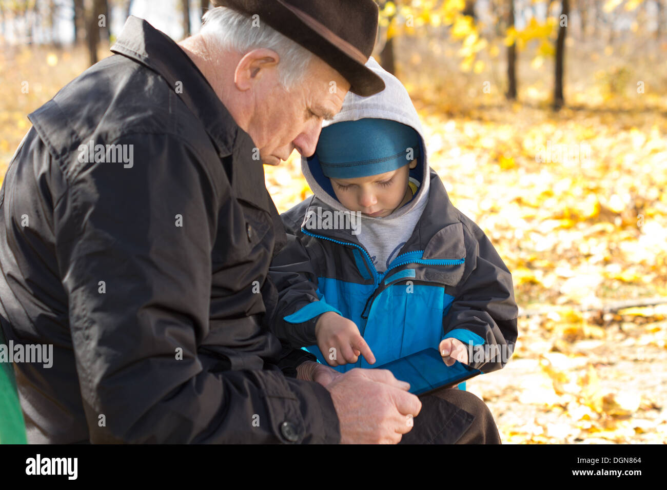 Grand-père et petit-fils le partage d'un ordinateur tablette assis ensemble sur un banc de parc de la navigation sur internet Banque D'Images
