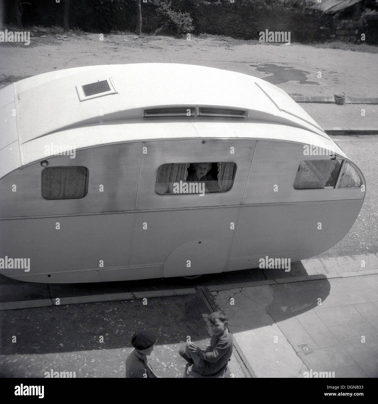 Photo historique,années 50 d'une forme inhabituelle caravane garé dans une rue latérale en France, avec dame à la fenêtre de chez les garçons. Banque D'Images