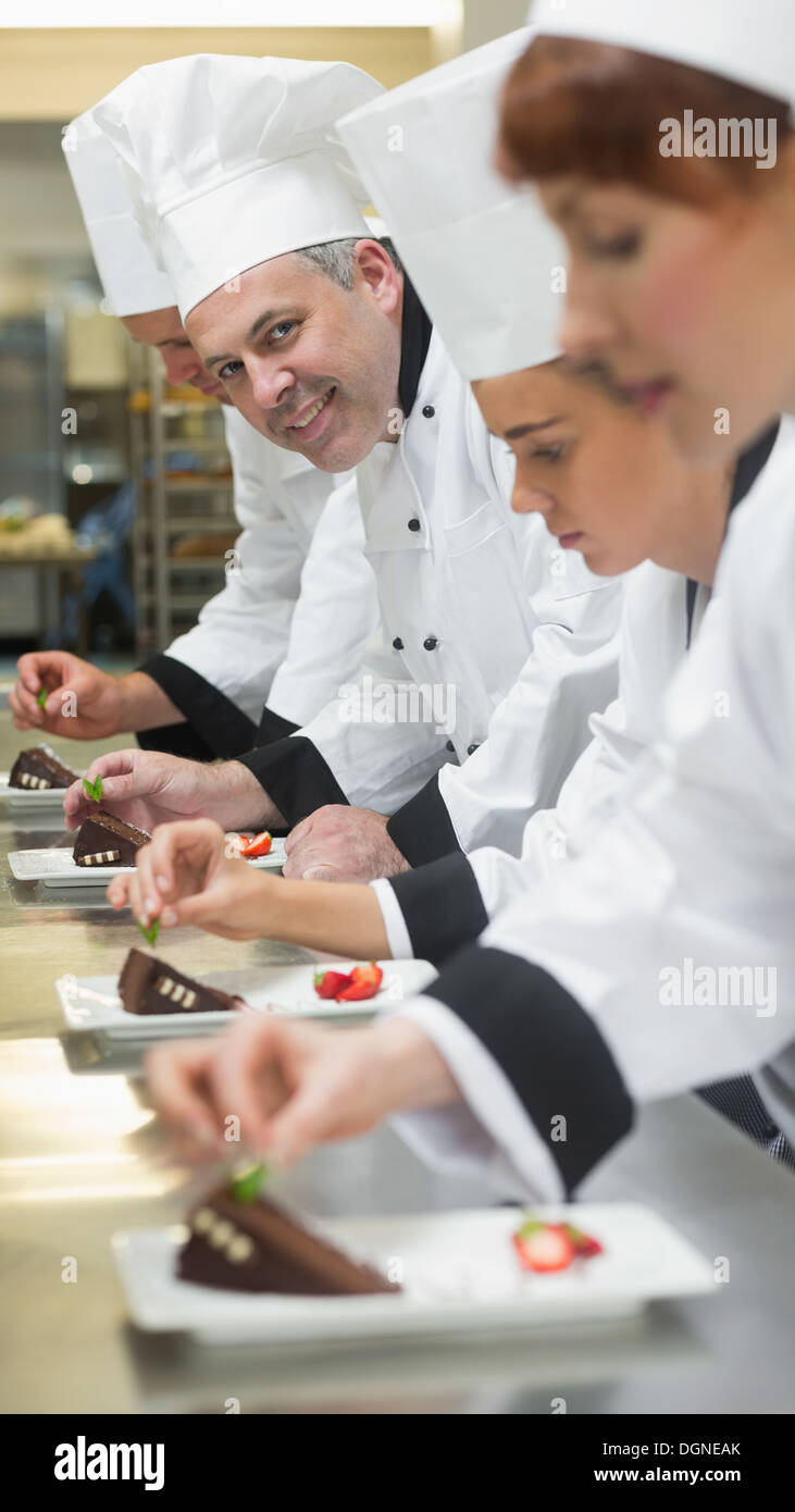 Équipe de cuisiniers dans une rangée de garnir les assiettes à dessert un smiling at camera Banque D'Images