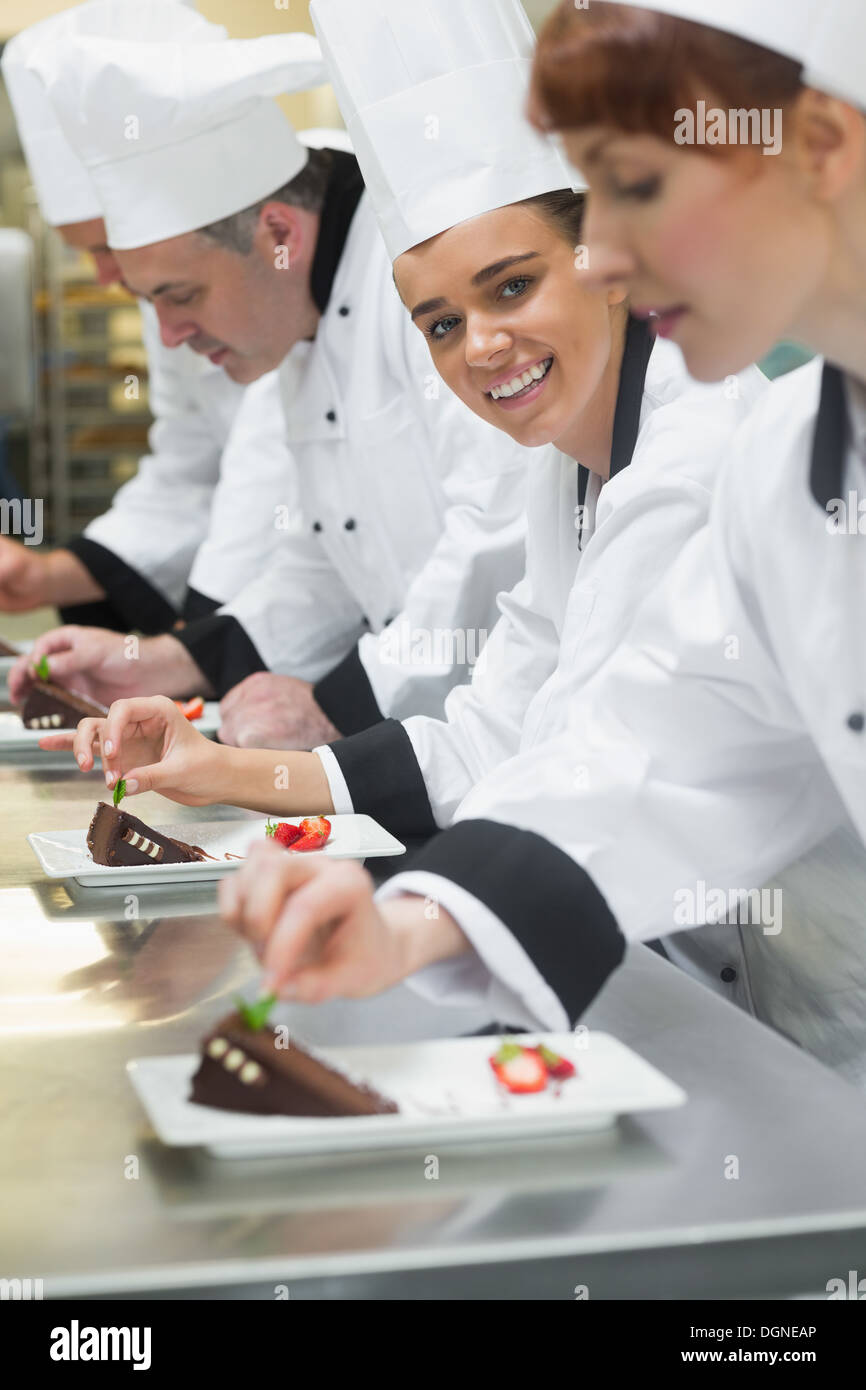 Équipe de cuisiniers dans une rangée de garnir les assiettes à dessert un girl smiling at camera Banque D'Images