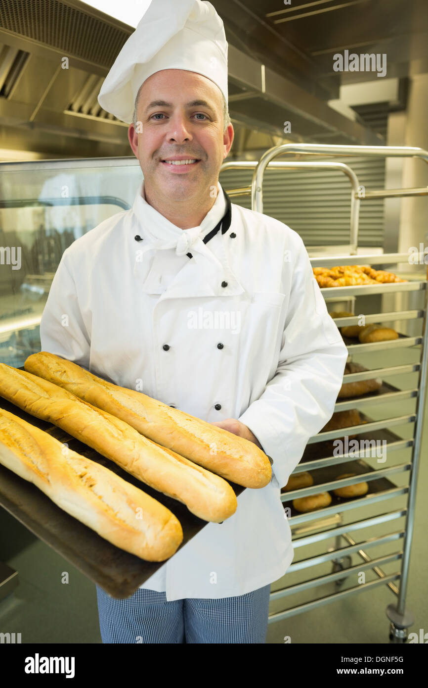 Baker mature présentant fièrement quelques baguettes sur une plaque de cuisson Banque D'Images
