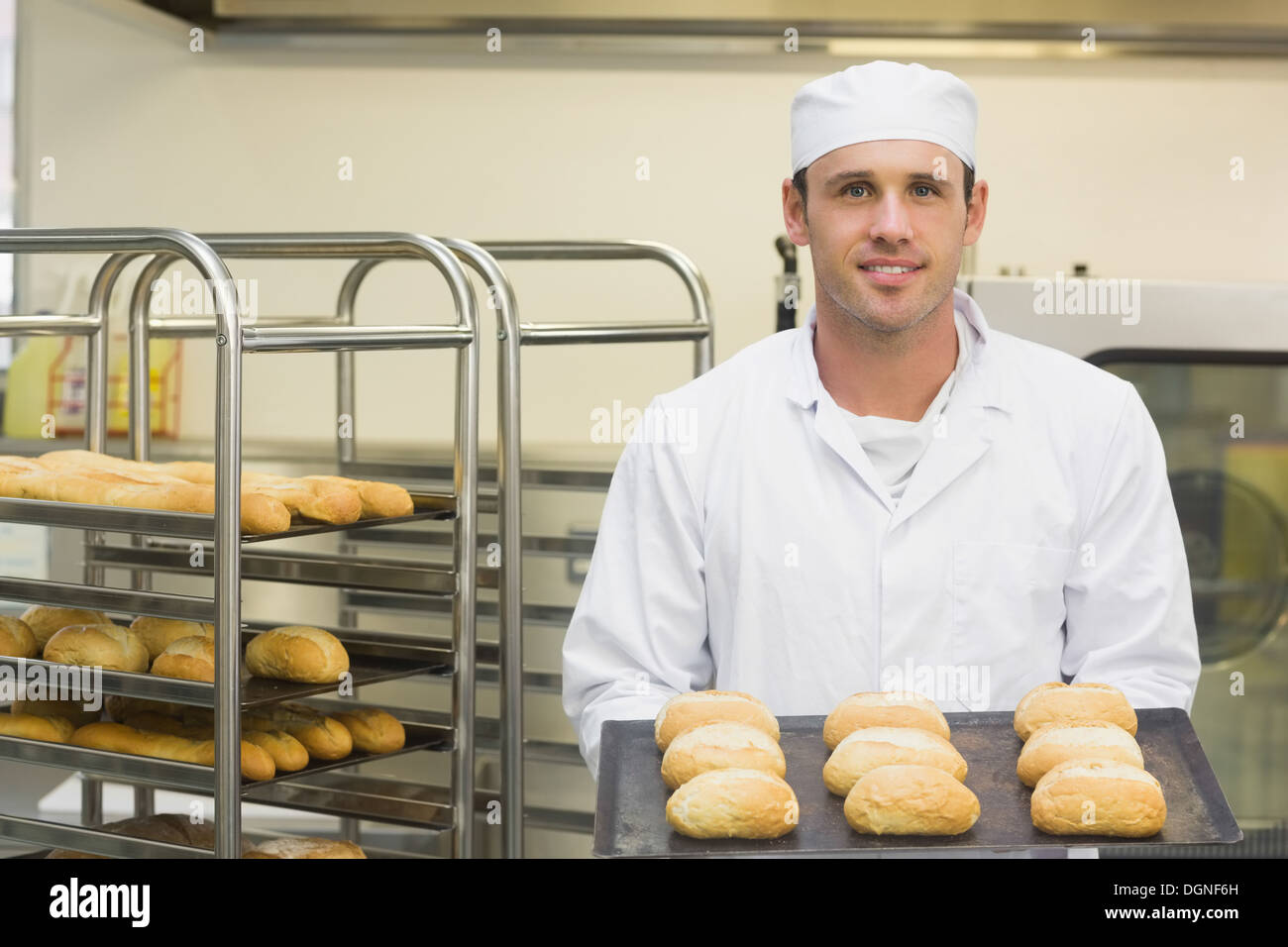 Happy young baker holding quelques rouleaux sur une plaque à pâtisserie Banque D'Images
