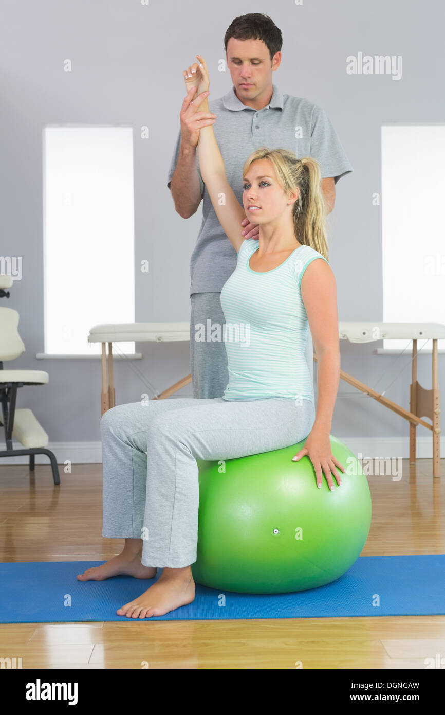 Physiothérapeute corriger patient assis sur la boule d'exercice Banque D'Images