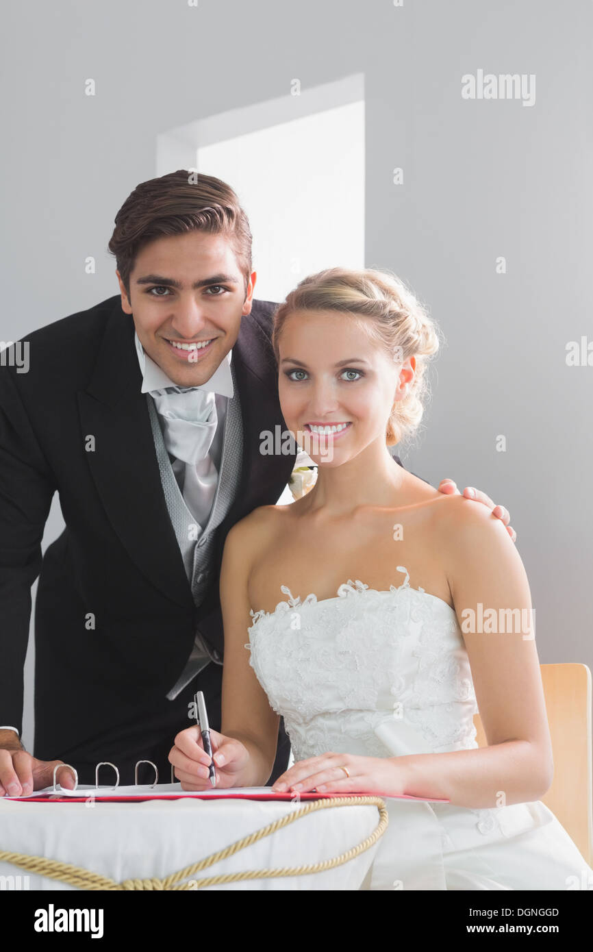 Deux jeunes mariés sitting at table signing wedding register Banque D'Images