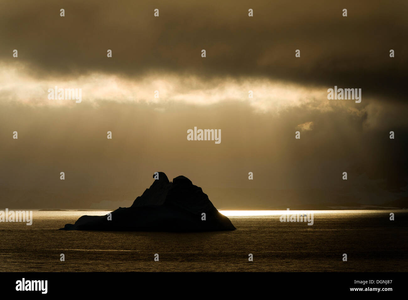 La lumière du soleil qui brillait à travers un trou dans les nuages, silhouette d'un iceberg à l'avant, le Canal Errera, péninsule Arctowski Banque D'Images