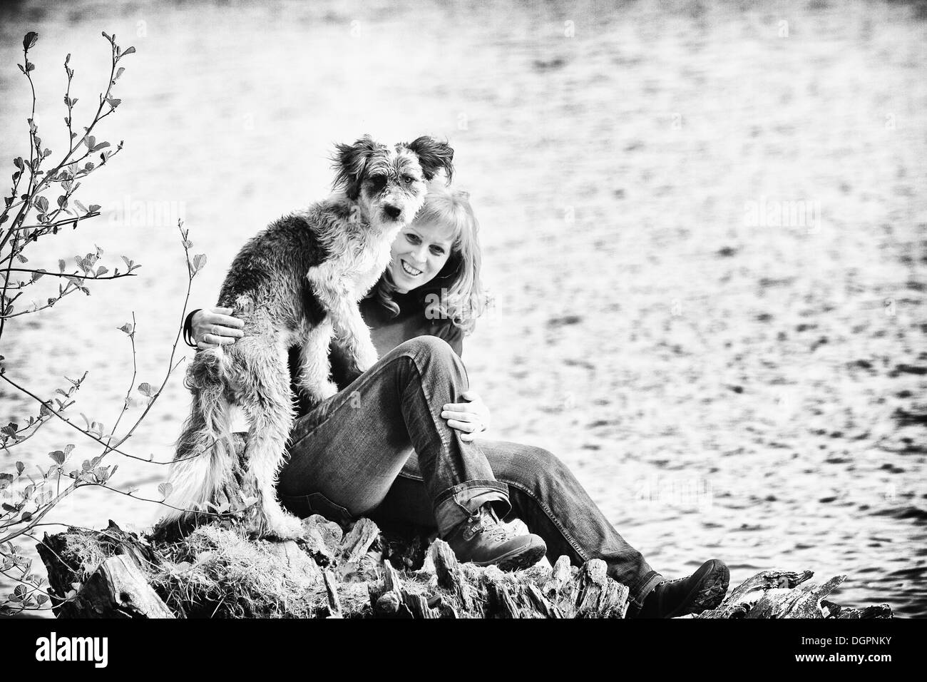 Femme assise avec son chien sur un rocher au bord d'un lac Banque D'Images