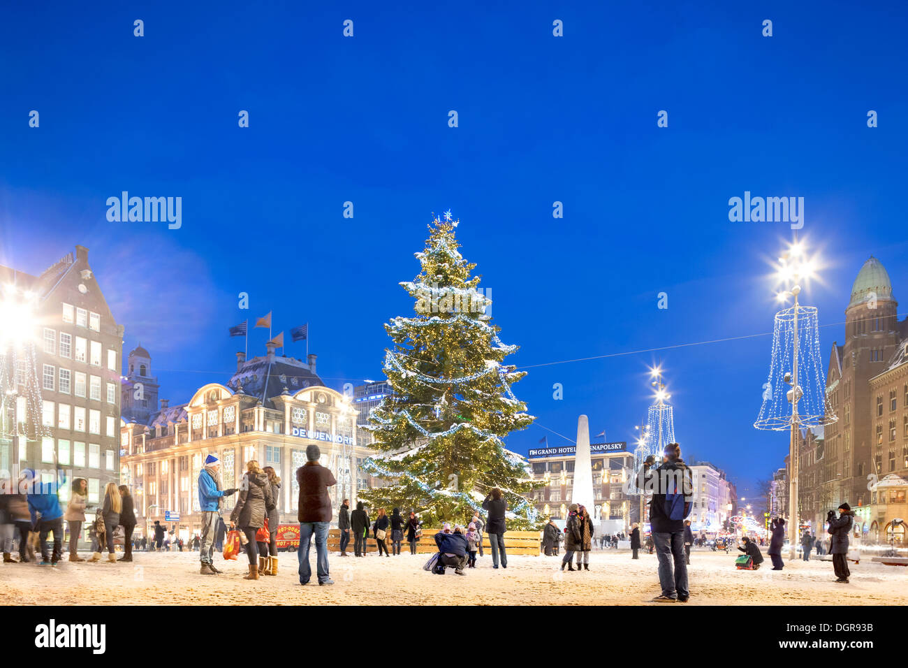 L'arbre de Noël d'Amsterdam w neige, feux de Noël sur la place du Dam avec les gens, touristes, visiteurs, poser et prendre des photos au crépuscule Banque D'Images