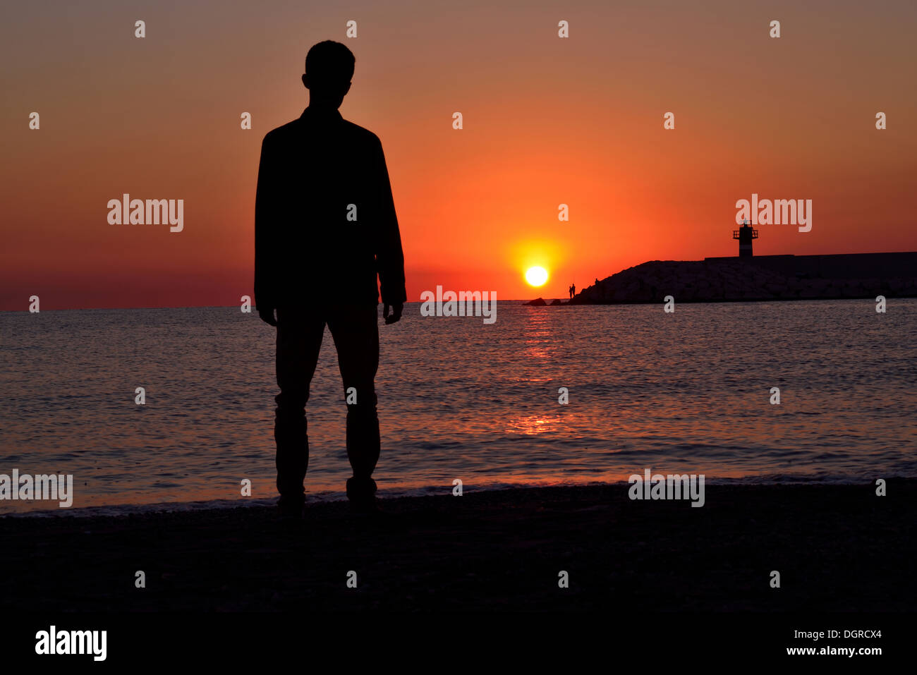 Silhouette de jeune standing on beach at sunset Banque D'Images