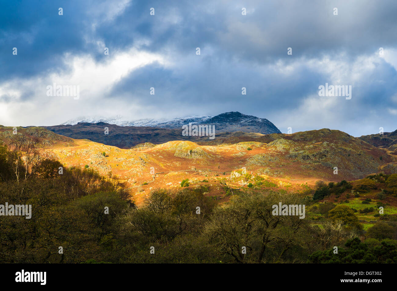 La lumière du soleil sur les collines et une tête de neige Scafell Pike vu de l'Eskdale Valley dans le Lake District, Cumbria, Angleterre. Banque D'Images