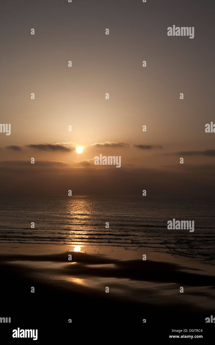 Coucher de soleil sur la mer juste au-dessus de l'horizon avec une plage au premier plan Sidi Ifni Maroc Banque D'Images