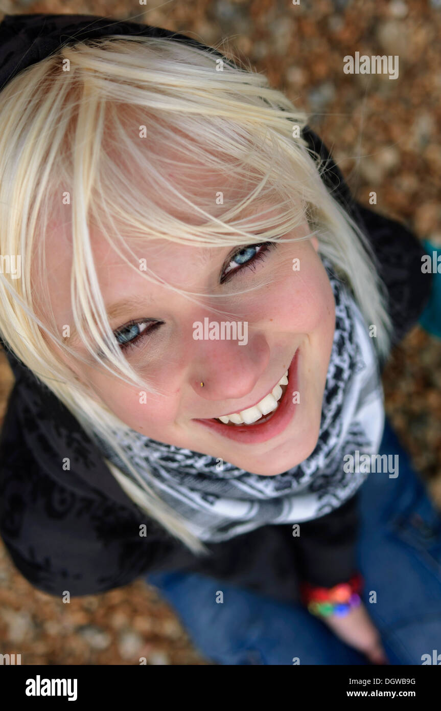 Adolescente blonde assise sur une plage de galets et à la recherche à l'appareil photo Banque D'Images