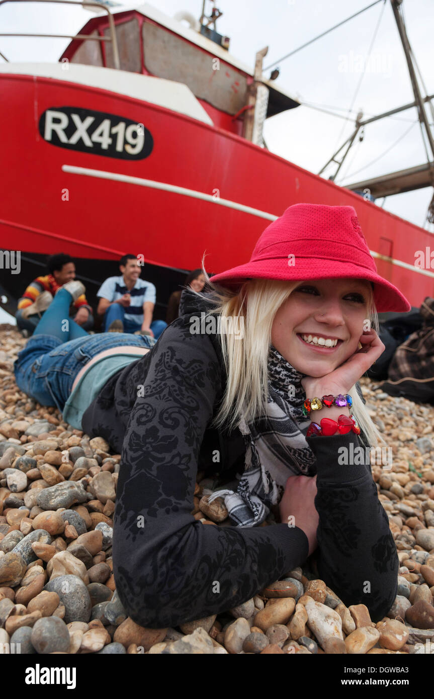 Adolescente blonde allongé sur une plage de galets avec des amis smiling at the camera Banque D'Images