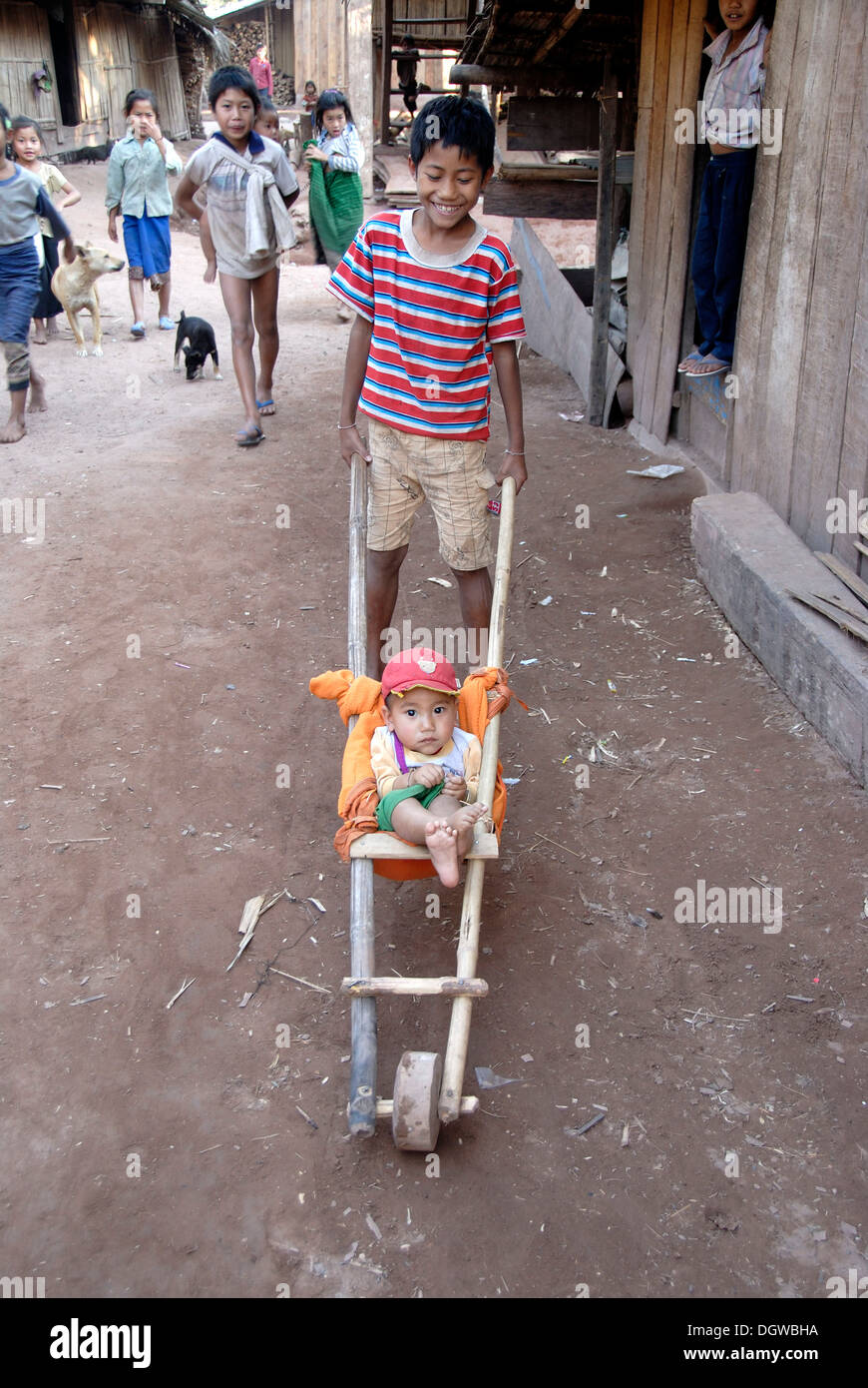 La pauvreté, les enfants qui jouent, poussant un bambin garçon dans un self-made-brouette, village de Ban Hathin Banque D'Images