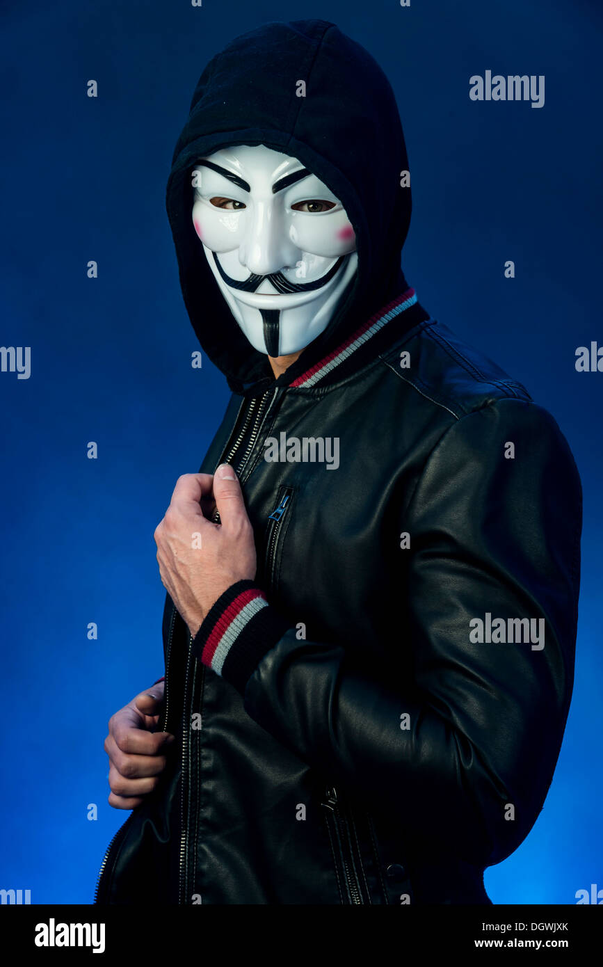 Jeune homme portant un masque anonyme avec un capuchon et une veste en cuir noir Banque D'Images