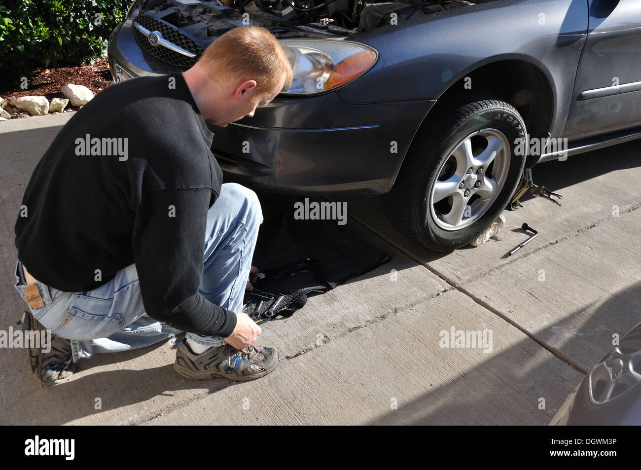 L'homme travaillant sur sa voiture dans son allée près de sa maison Banque D'Images