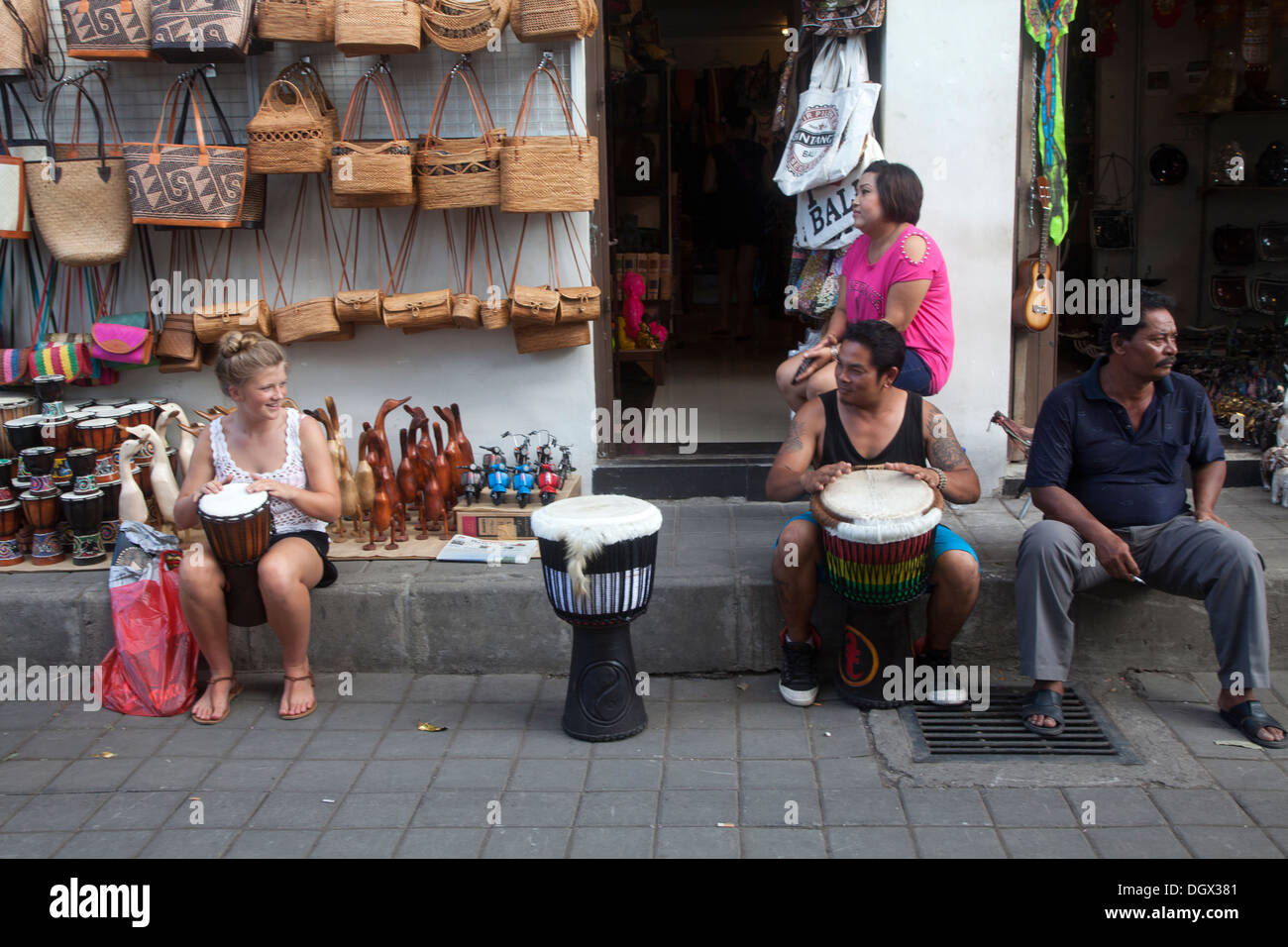 Fille touristiques Indonesian man jouer drum Ubud Bali jouer profiter de profiter de la musique enjouée de l'Indonésie d'open market boutique cadeaux Boutique sacs Banque D'Images