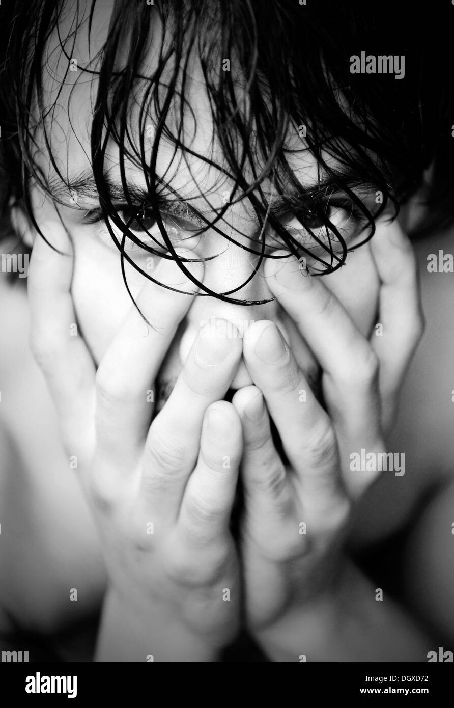Jeune homme avec les cheveux mouillés et ses mains sur son visage Banque D'Images