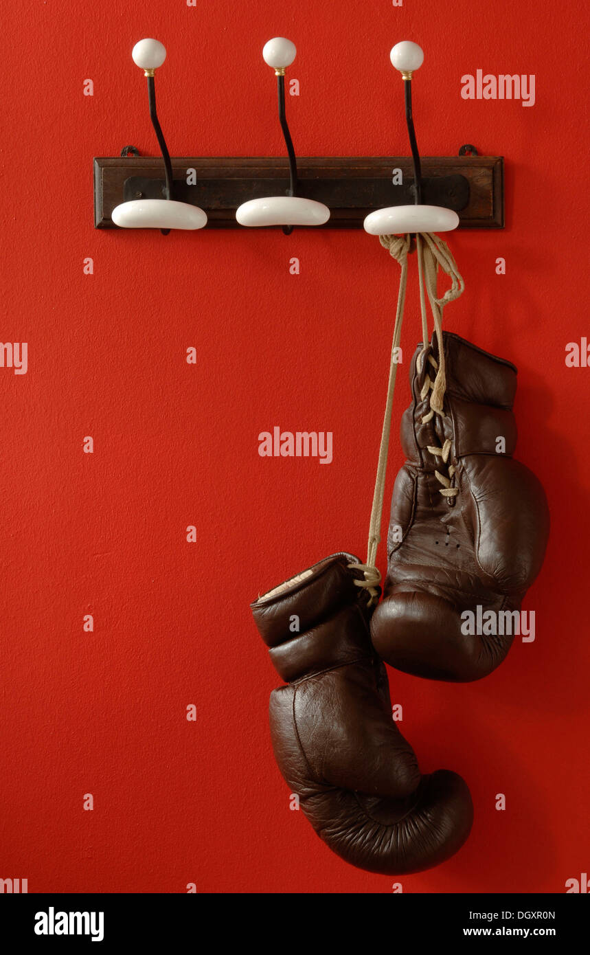 Gants de boxe suspendu à des crochets à vêtements nostalgique sur un mur rouge Banque D'Images