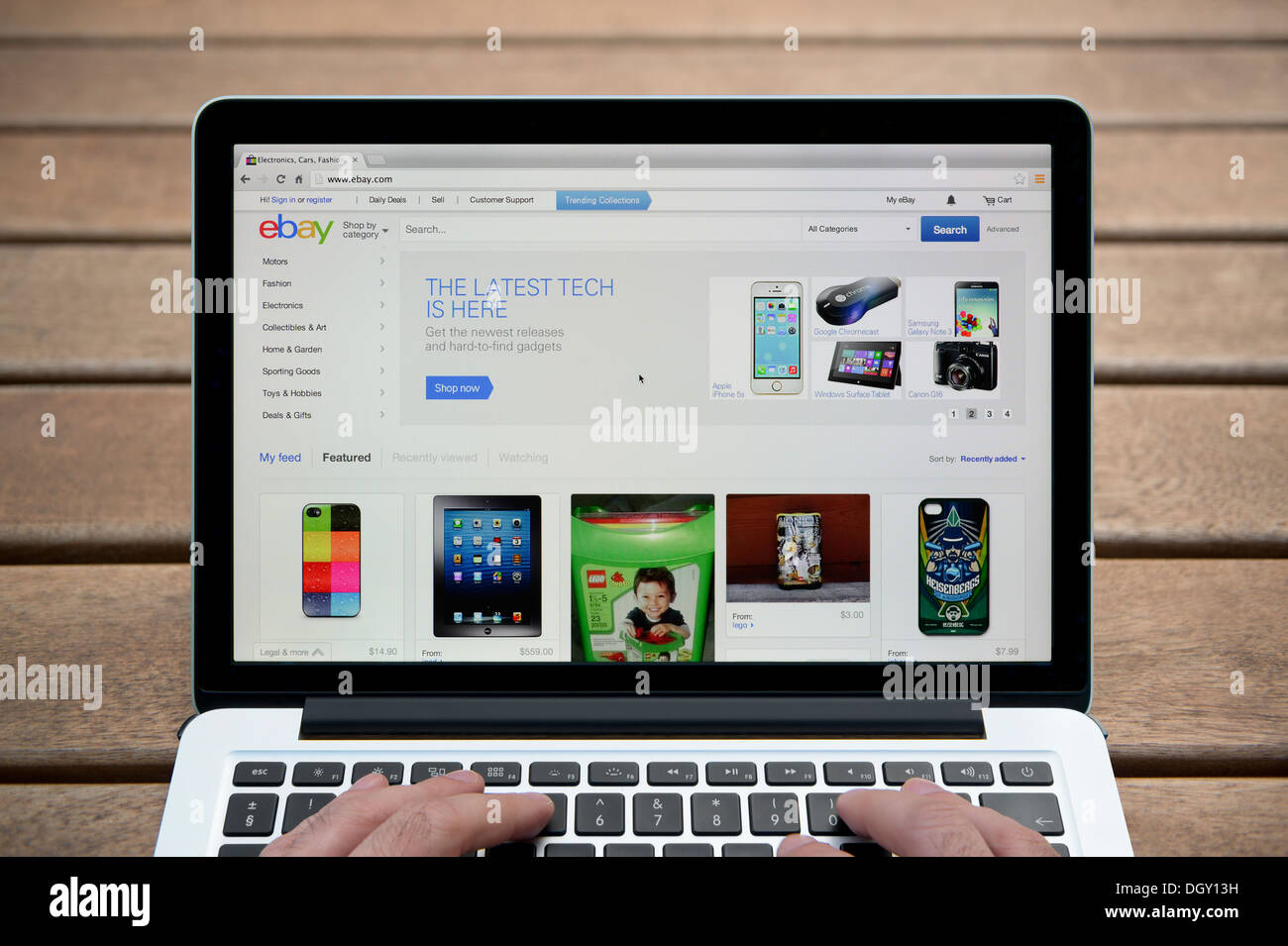 Le site web d'ebay sur un MacBook contre un banc en bois fond de plein air y compris les doigts d'un homme (usage éditorial uniquement). Banque D'Images