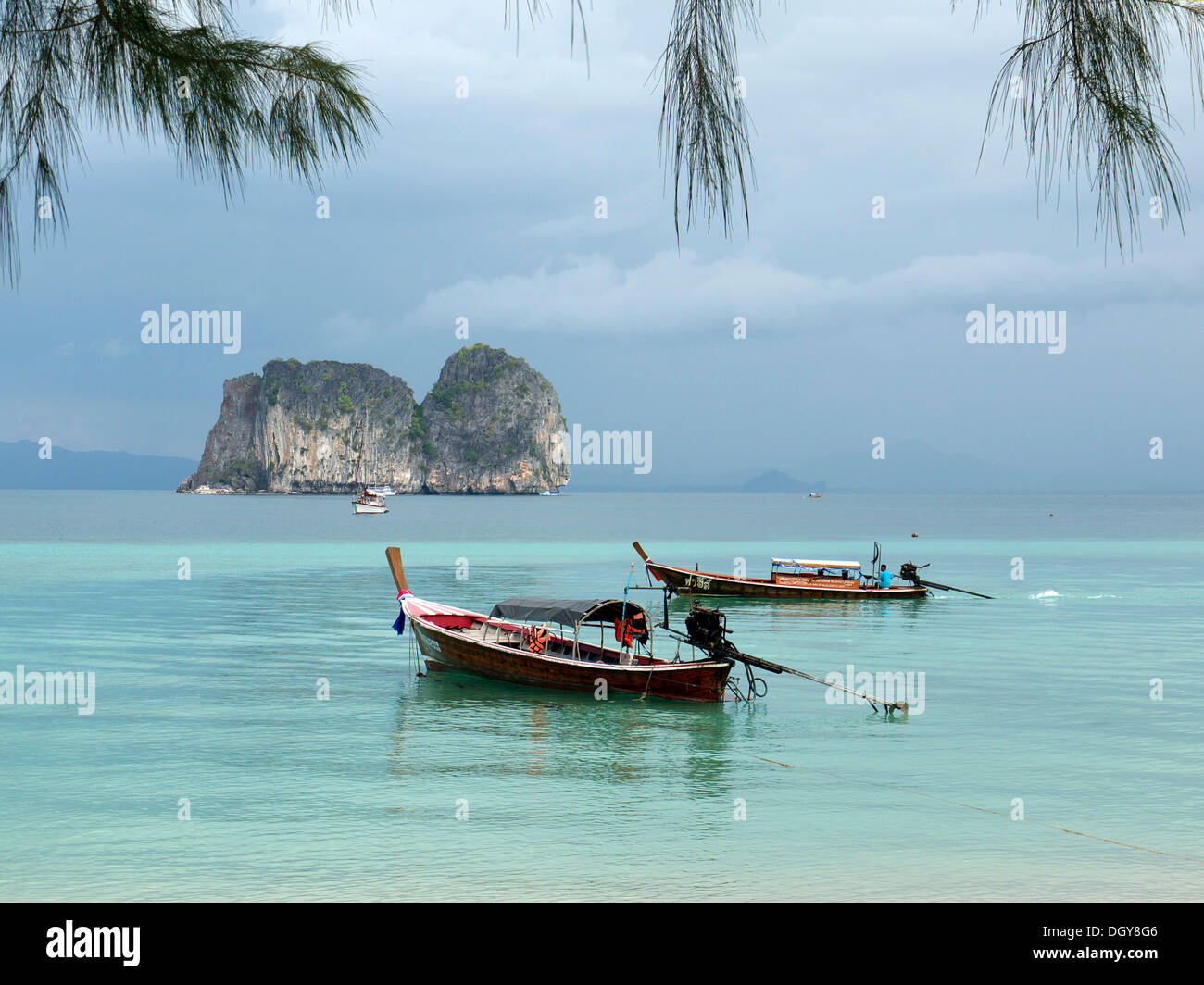 Longue queue bateaux dans une mer cristalline, à l'arrière d'un groupe de roches, vu de l'île de Hai Ko, Ko Ngai, la mer d'Andaman Banque D'Images