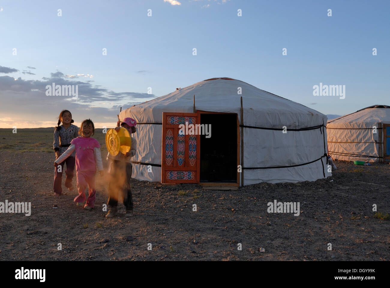 Enfants mongols et fille européenne jouant avec un tambour en plastique jaune en face d'une yourte ou ger mongole, désert de Gobi Banque D'Images