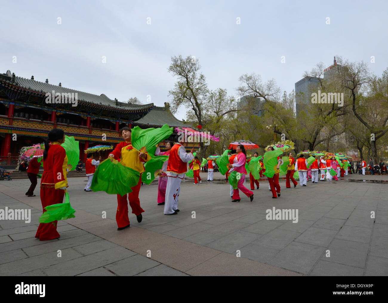 Danseurs amateurs chinois dans un parc public en face d'immeubles de grande hauteur et un pavillon chinois, Urumqi Banque D'Images