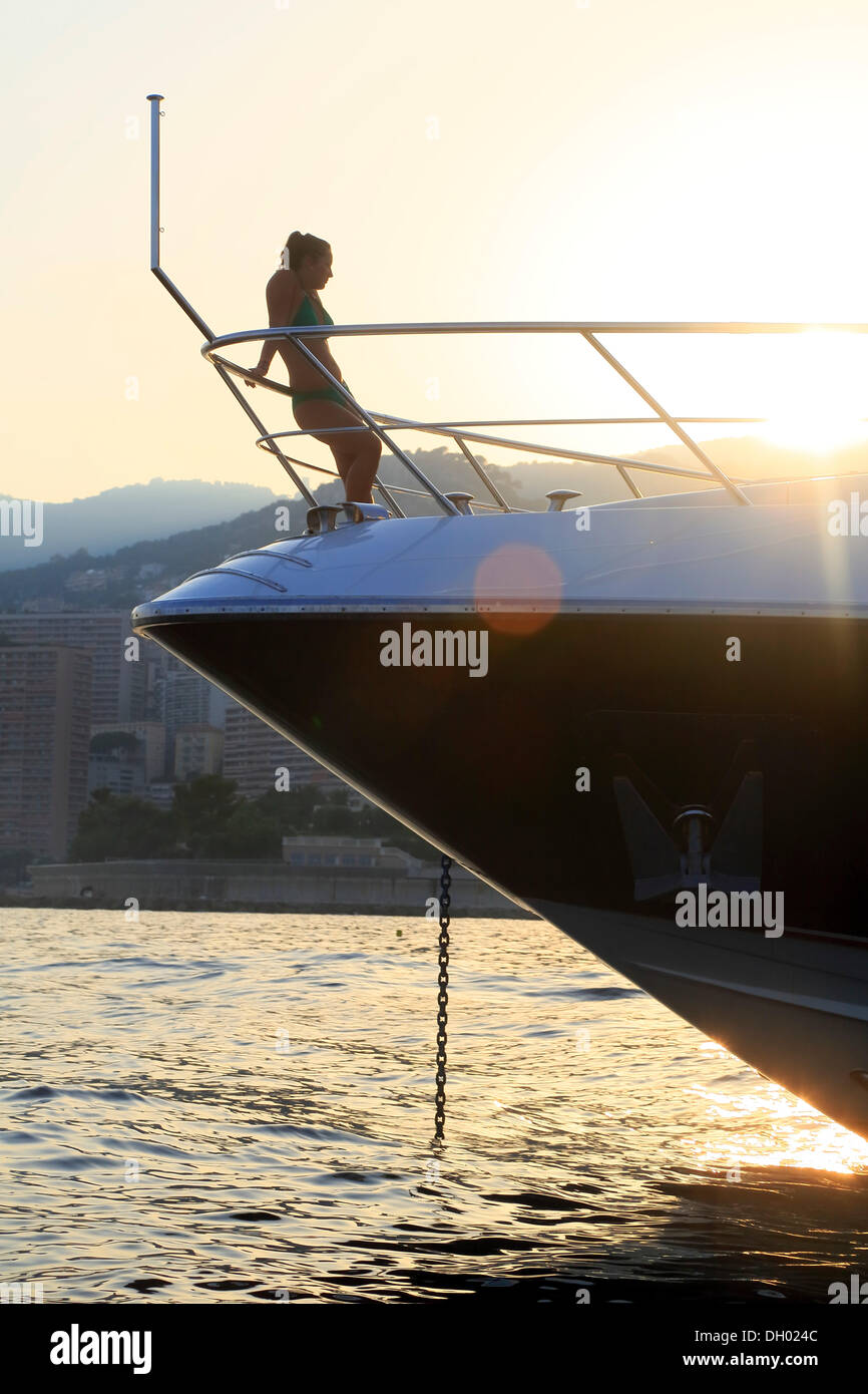 Jeune femme appuyée contre la rambarde de l'arc d'un yacht à moteur dans la soirée avec le rétroéclairage, Principauté de Monaco Banque D'Images