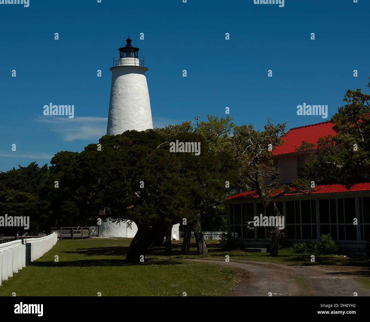 Ocracoke Island Lighthouse derrière les arbres avec la clôture blanche et du toit de la maison montrant. Banque D'Images