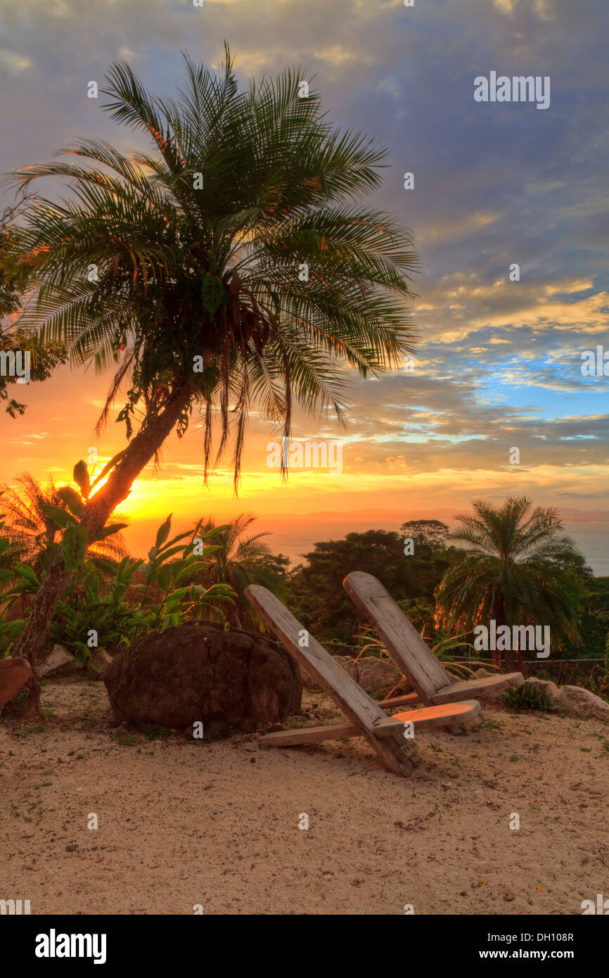 Chaises vides sous un palmier avec vue sur l'océan Pacifique et la Péninsule de Nicoya au coucher du soleil près de Herradura, Costa Rica (HDR) Banque D'Images