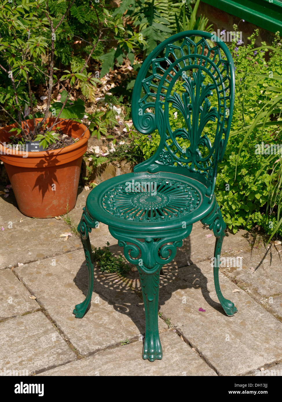 Peint vert fauteuil de jardin en métal ouvragé sur slabbed patio, Jardins Barnsdale, Oakham, Rutland, England, UK. Banque D'Images